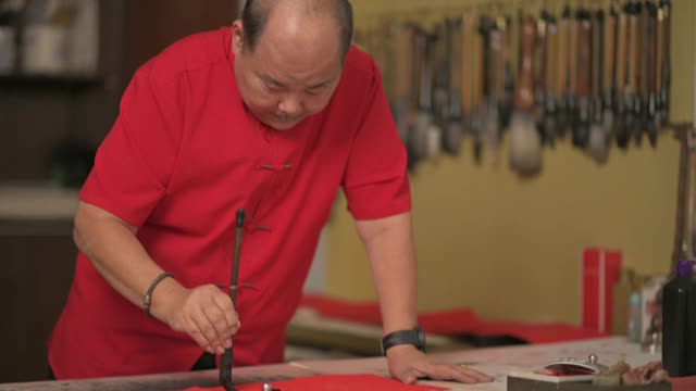 亚洲华人男性练习书法，为即将到来的中国新年庆祝家庭装饰目的与繁荣和良好的措辞写在一张红色的纸上视频素材