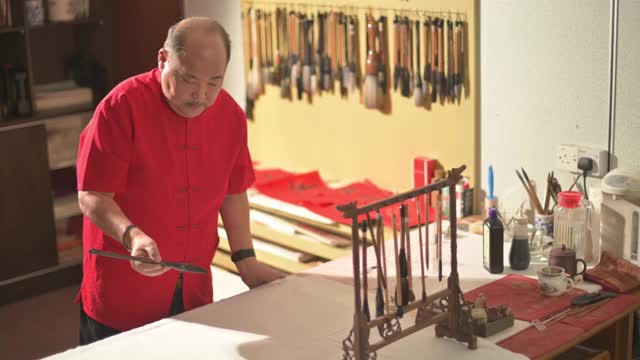 亚洲华人男性练习书法，为即将到来的中国新年庆祝家庭装饰目的与繁荣和良好的措辞写在一张红色的纸上视频素材