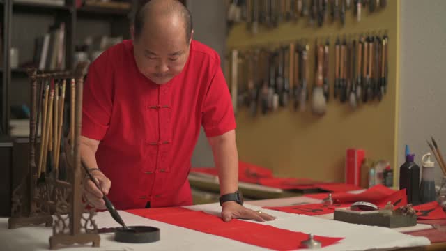 亚洲华人男性练习书法，为即将到来的中国新年庆祝家庭装饰目的与繁荣和良好的措辞写在一张红色的纸上视频素材