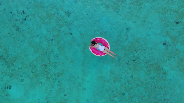 鸟瞰图一个迷人的女人浮动与游泳环在水晶清澈的大海视频素材