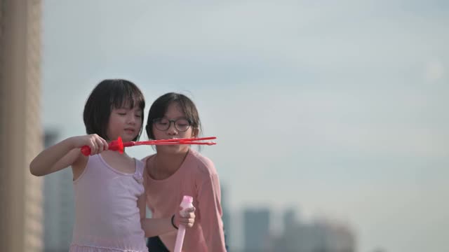 亚洲华人的兄弟姐妹年轻的女孩妹妹玩泡泡在晚上日落户外视频素材