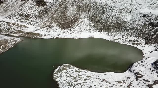 无人机拍摄到奥地利费尔德西科普夫附近的一个心形湖泊。湖被雪包围，部分覆盖了阿尔卑斯山脉的石坡。这个湖被陡峭的山峰包围着视频素材