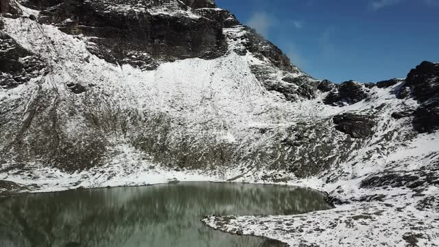 无人机拍摄到奥地利费尔德西科普夫附近的一个心形湖泊。湖被雪包围，部分覆盖了阿尔卑斯山脉的石坡。这个湖被陡峭的山峰包围着视频素材