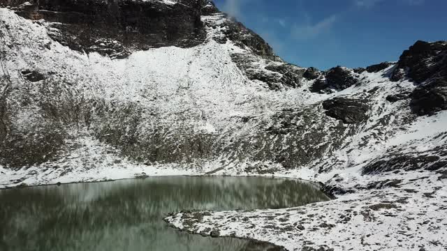 无人机拍摄到奥地利费尔德西科普夫附近的一个心形湖泊。湖被雪包围，部分覆盖了阿尔卑斯山脉的石坡。这个湖被陡峭的山峰包围着视频素材