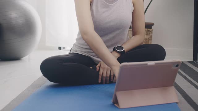 亚洲女性使用智能手表后玩瑜伽和锻炼在家里的背景。运动减肥，增加灵活性和收紧形状。4 k慢动作。视频素材