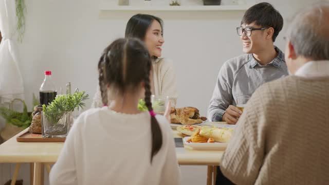 快乐的亚洲家庭共进早餐。快乐的父母，爷爷和可爱的女儿在家里的餐桌上一起享用早餐和祝酒。美妙的时刻家庭视频素材