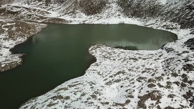 无人机拍摄到奥地利费尔德西科普夫附近的一个心形湖泊。湖被雪包围，部分覆盖了阿尔卑斯山脉的石坡。这个湖被陡峭的山峰包围着视频素材