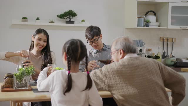 远景:快乐的亚洲家庭一起享用早餐。快乐的父母，爷爷和可爱的女儿在家里的餐桌上一起享用早餐。美妙的时刻家庭视频素材