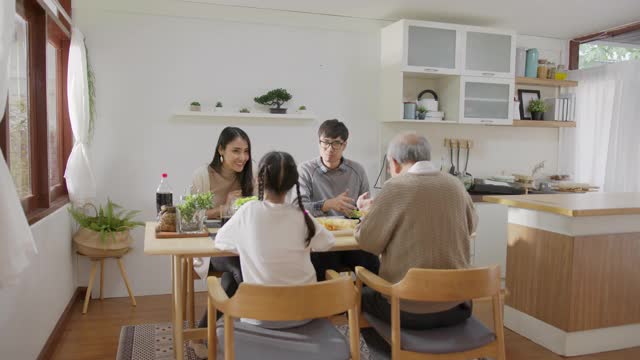 远景:快乐的亚洲家庭一起享用早餐。快乐的父母，爷爷和可爱的女儿在家里的餐桌上一起享用早餐。美妙的时刻家庭视频素材