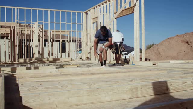 一名年轻的木匠建筑工人正在工地上建造一所住宅，他正在用气枪将一堵木框墙垂直地竖起来视频素材