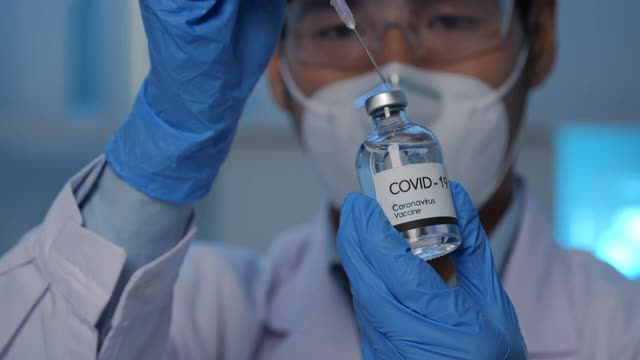 专业科学家拿着注射器从Covid - 19瓶中吸取液体在实验室中测试和分析数据。视频素材