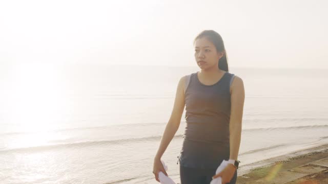 亚洲妇女在晨曦的背景下，在海边跑步后热身运动。4 k慢动作。视频素材