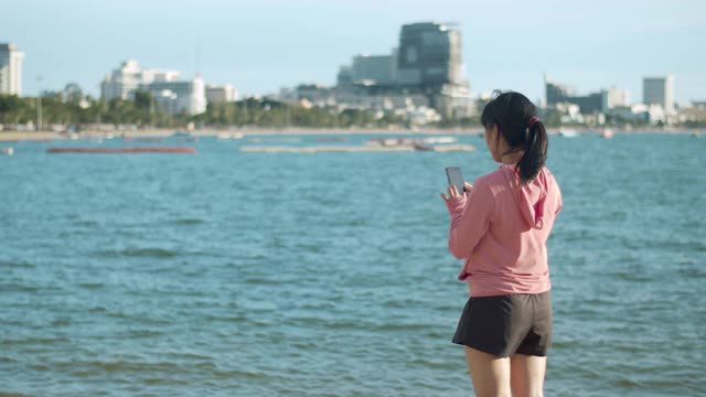 美丽的运动女孩使用智能手机视频聊天后，站在海滩上跑步。视频素材