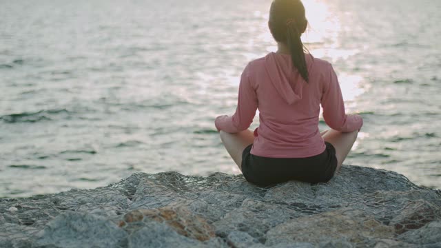 运动亚洲女性坐在冥想姿势姿势医学瑜伽调息平衡在美丽的海滩景色在日出。视频素材