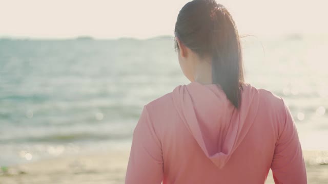 快乐的女运动员放松地享受着宁静的日落，抬头呼吸着新鲜的空气，放松着美丽的风景和海景。视频素材