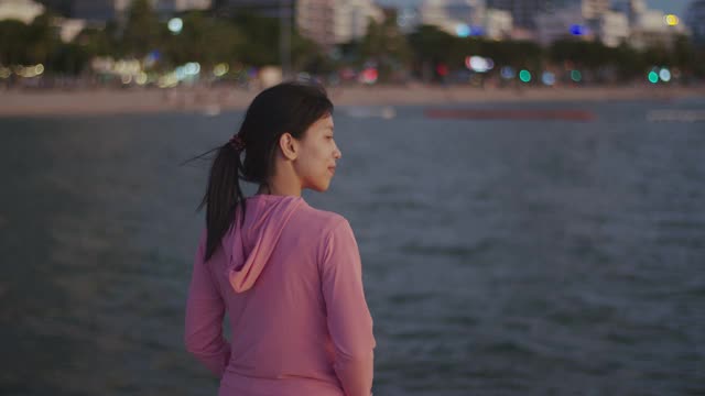 一位美丽的亚洲女跑步者站在沙滩上看海景。视频素材