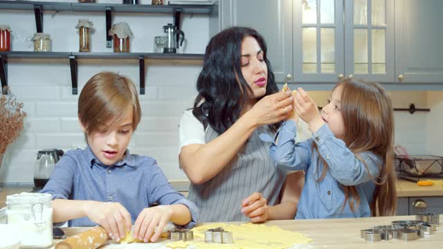 幸福的家庭年轻的妈妈和两个可爱的孩子一起在厨房里做饼干的时候玩得很开心。视频素材