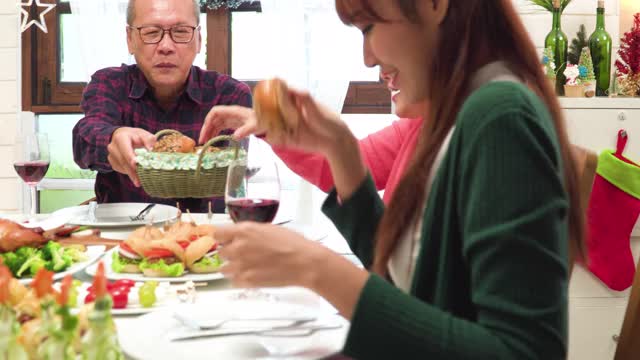 在12月的圣诞节庆祝活动中，东南亚多代同堂的家庭围坐在一张可爱的餐桌前。爷爷和孙女分享面包，孙子在家里装饰着圣诞树和装饰品。视频素材