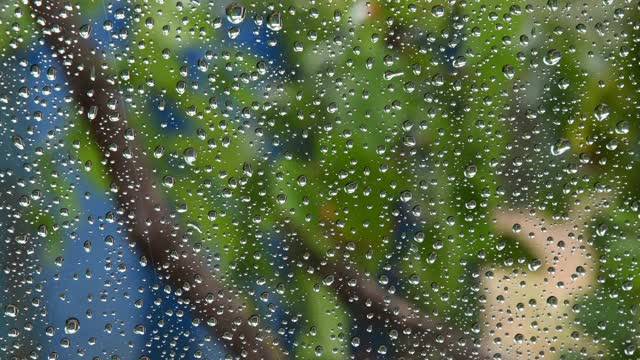 雨滴落在透明的玻璃表面，后面模糊的运动视频素材