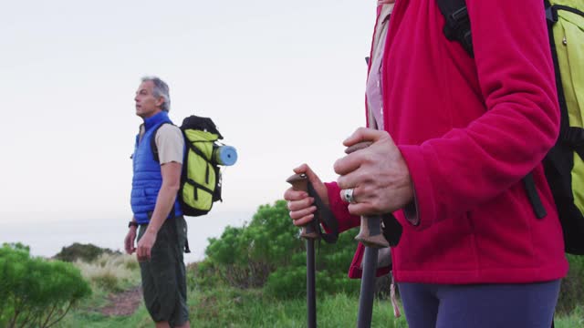 一对背着背包、拄着登山杖的资深徒步情侣站在一起看着对方视频素材