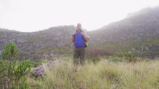 一个背着背包的老徒步者站在山上的草地上。徒步旅行视频素材