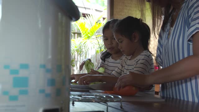 两个可爱的亚洲女孩和妈妈一起在厨房里准备食材，然后一起做蔬菜视频素材