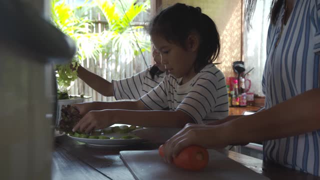 两个可爱的亚洲女孩和妈妈一起在厨房里准备食材，然后一起做蔬菜视频素材