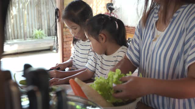 两个可爱的亚洲女孩和妈妈一起在厨房里准备食材，然后一起做蔬菜视频素材