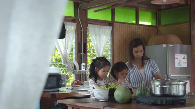 两个可爱的亚洲女孩和妈妈一起在厨房里准备食材，然后一起做蔬菜视频素材