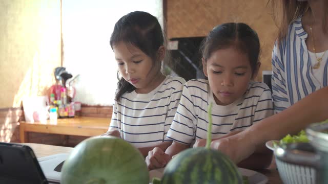 两个可爱的亚洲女孩和妈妈一起在厨房里准备食材，然后一起做蔬菜视频素材