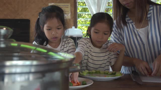 两个可爱的亚洲女孩和妈妈一起在厨房里准备食材，然后一起做蔬菜视频素材