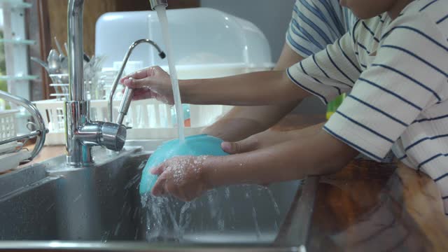 亚洲女孩和她的母亲一起在厨房里吃完饭后帮助清理和洗餐具。视频素材