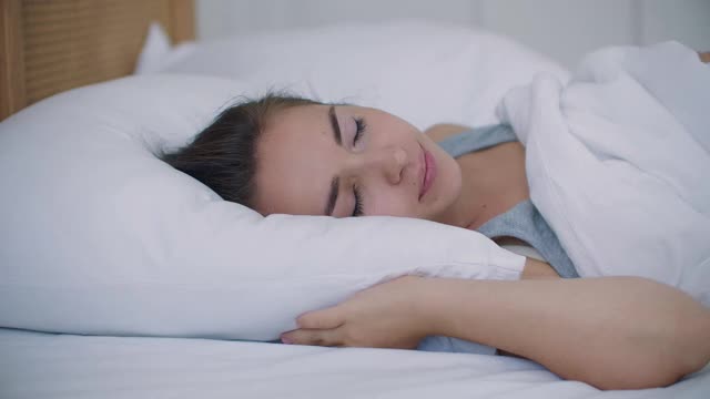 年轻女子用枕头捂住耳朵。被吵闹的邻居打扰，睡不着。烦躁的白人女孩失眠醒来。视频素材