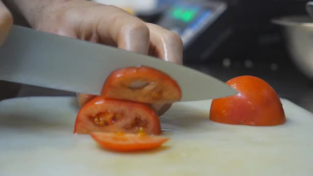 在厨房餐厅里，男厨师用刀在塑料切菜板上切一个新鲜的红番茄。制作健康蔬菜沙拉的过程。烹饪食物的概念。特写慢动作视频素材