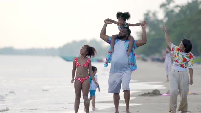 4K混合种族家庭假期快乐。一对父母和可爱的小女孩手牵着手一起在夏天的海滩上散步。父亲和母亲与两个女儿享受和有乐趣的海滩视频下载
