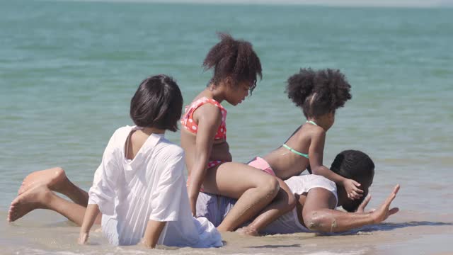 4K混合种族家庭假期快乐。夏天，父母带着两个女儿坐在沙滩上玩海水。爸爸和妈妈与可爱的孩子女孩享受和有乐趣的暑假视频下载