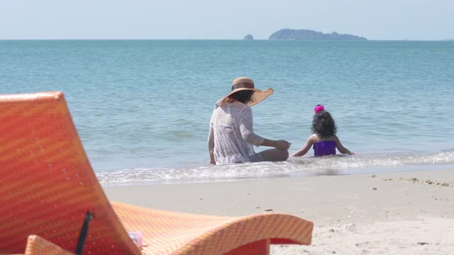 4K亚洲家庭假期快乐。美丽的亚洲母亲坐在海滩上和小女儿玩海水在夏天的一天。可爱的小女孩放松和有乐趣的妈妈在夏季旅游旅行。视频下载