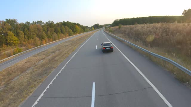 鸟瞰图的黑色汽车行驶在乡村道路上。在旅途中沿着高速公路行驶的汽车。在高速公路上飞驰的汽车。自由和冒险的旅游理念。后视图视频素材