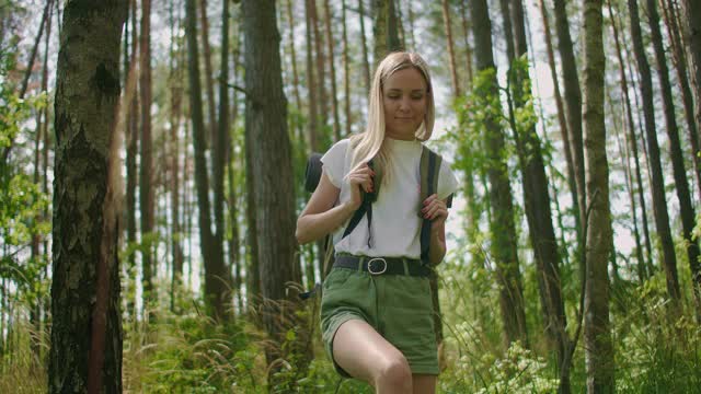 慢镜头的一个女人走在森林道路与一个背包通过松林穿过草地视频素材