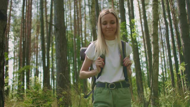 慢镜头的一个女人走在森林道路与一个背包通过松林穿过草地视频素材