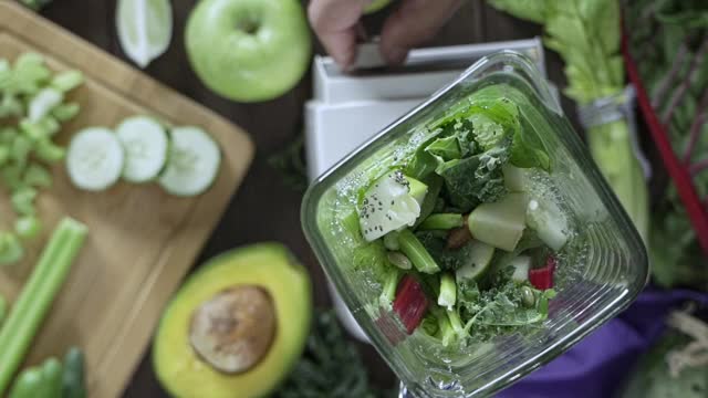 饮食概念:慢动作直接下镜头的搅拌机混合蔬菜和水果排毒奶昔。厨房桌上的切菜板和搅拌机搅拌视频素材