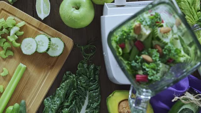 饮食概念:直接向下平移视图拍摄的女人的手切蔬菜排毒奶昔。厨房桌上的切菜板和搅拌机视频素材