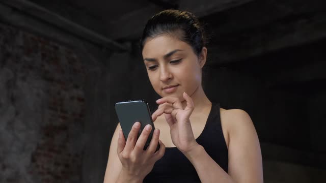 A Portrait Of Young Girl Or Woman With Smartphone In A Gym.一个年轻的印度女人在健身房用智能手机锻炼训练的特写视频素材