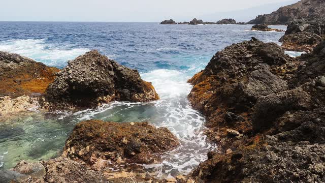 蓝绿色的海浪撞击着海岸附近的火山岩。视频素材