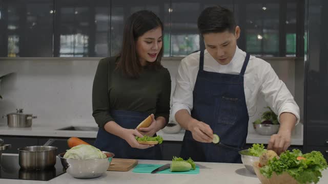 年轻的亚洲夫妇烹饪晚餐在现代厨房享受一起做的汉堡包。丈夫和妻子的笑容清新活泼。生活方式奢侈舒适。爱，幸福家庭理念。视频素材