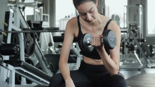 美丽的运动女人在健身房里用哑铃锻炼。视频素材