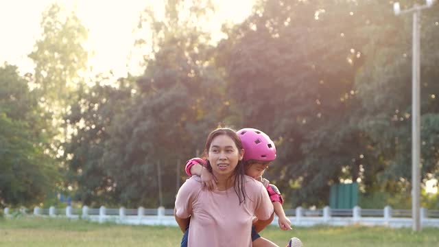 可爱的小女儿骑着她的妈妈在夏天的草地上。全家人一起度假。视频素材