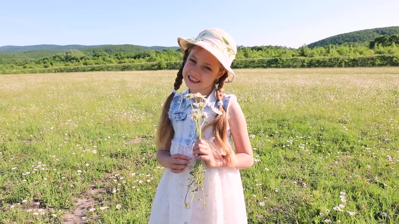 阳光明媚的夏天。漂亮的小女孩穿着裙子，手里拿着一束雏菊。孩子和野花。视频素材