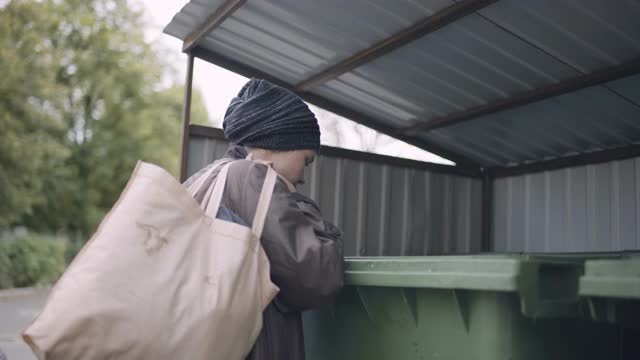 流浪汉在户外吃着垃圾桶里的面包，饥饿的无家可归的女人视频素材