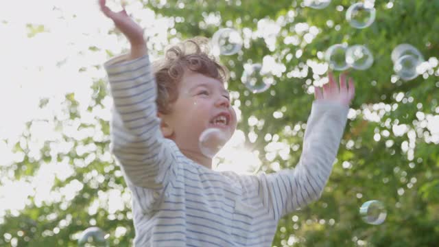 小男孩在花园里追逐和戳破泡泡视频素材